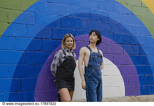 Friends standing by rainbow painted on wall