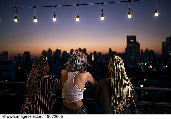 Friends standing under string lights on rooftop at dusk