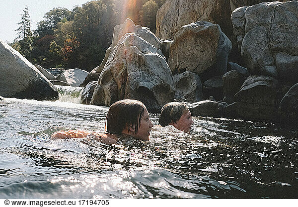 Friends Swim together next to a waterfall in the Yuba River