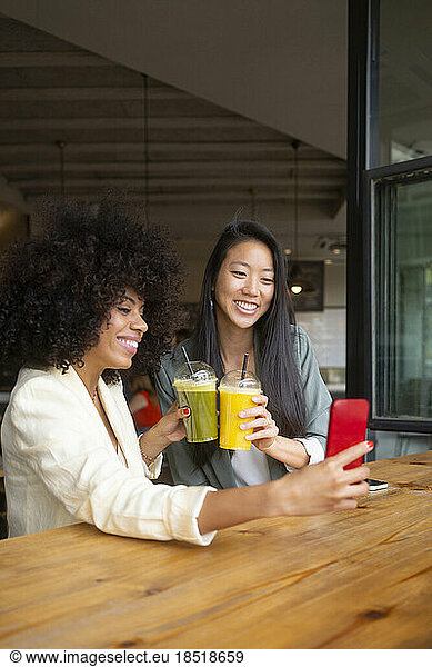 Friends taking selfie holding healthy drinks at cafe