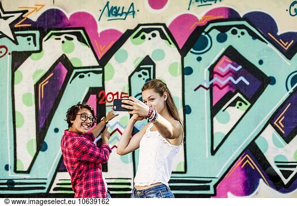 Friends taking selfie while standing against wall with graffiti