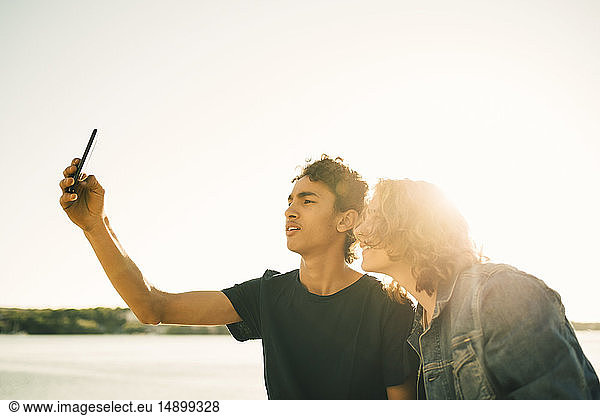 Friends taking selfie with mobile phone against clear sky in city during sunny day