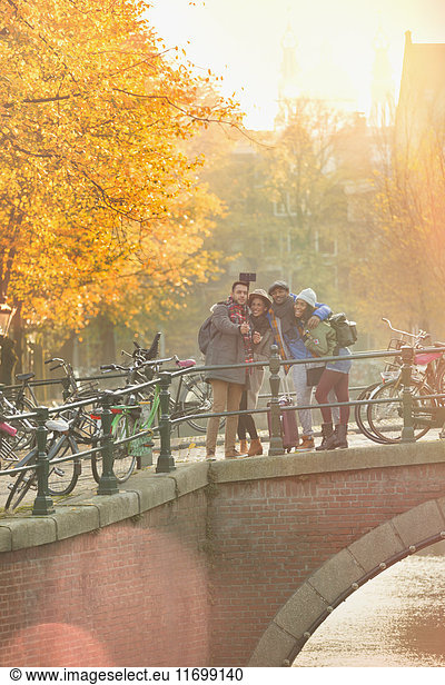 Friends taking selfie with selfie stick on autumn bridge over canal in Amsterdam