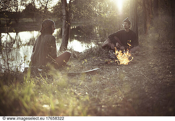 friends talk around fire in natural light by water