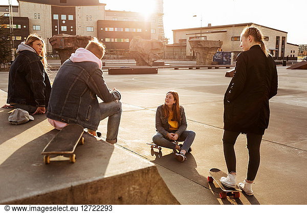 Friends talking while hanging out at skateboard park in city during sunny day