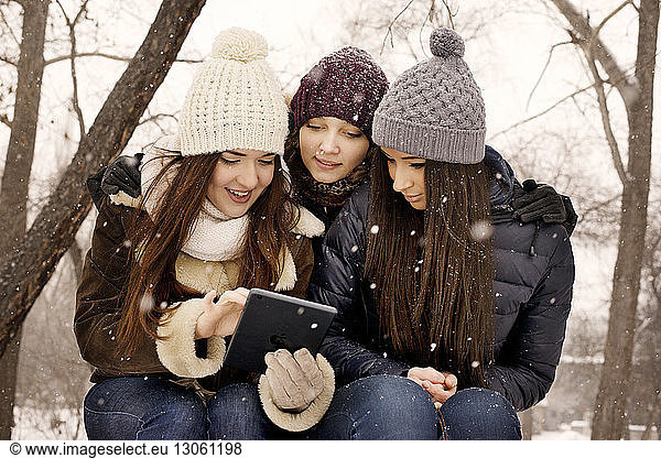 Friends using digital tablet in park during snowfall