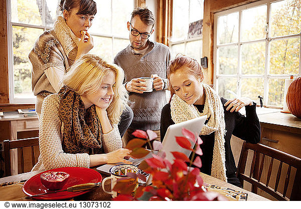 Friends using laptop computer at table in home