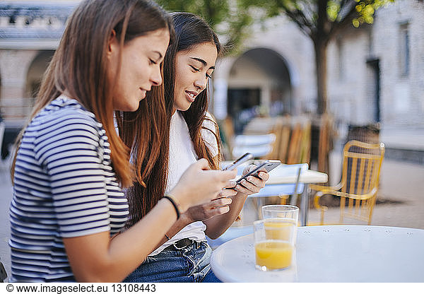 Friends using mobile phones while sitting at sidewalk cafe