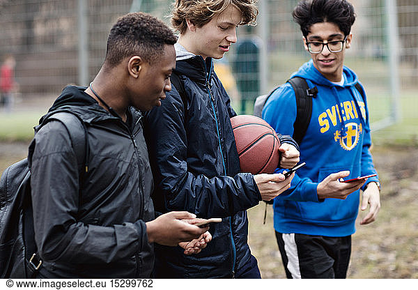 Friends using smart phones while walking on street after basketball practice