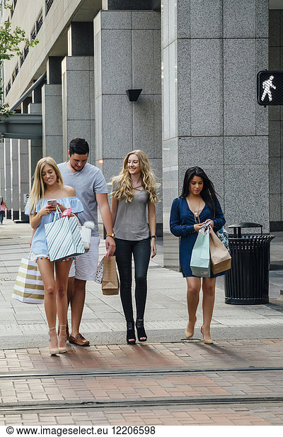 Friends walking in city carrying shopping bags texting on cell phones