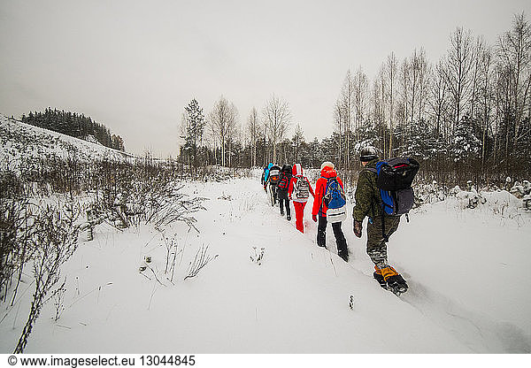 Friends walking on snowy field against sky