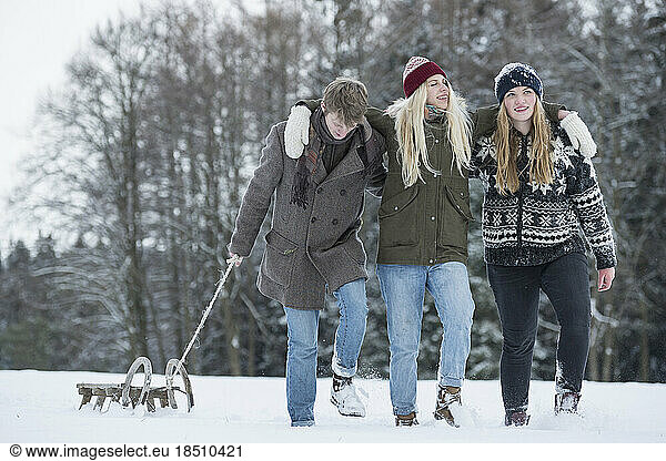 Friends walking with slide in snowy landscape in winter  Bavaria  Germany