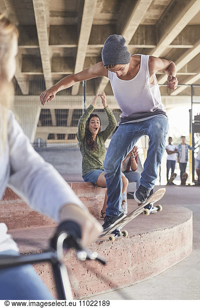 Friends watching teenage boy skateboarding at skate park