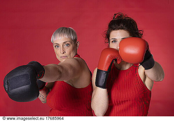 Friends wearing boxing gloves standing against red background