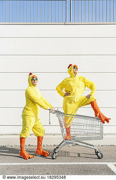 Friends wearing chicken costumes standing with shopping cart in front of wall
