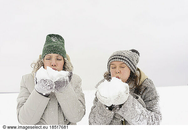 Friends wearing knit hats blowing snow in winter