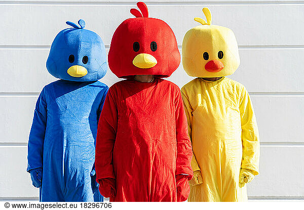 Friends wearing multi colored costumes standing in front of white wall