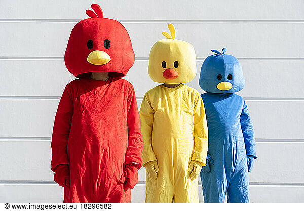 Friends wearing multi colored duck costumes standing in front of white wall
