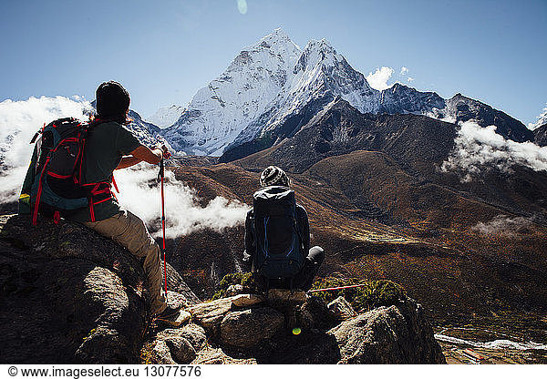 Friends with backpacks sitting on mountain against blue sky at Sagarmatha National Park