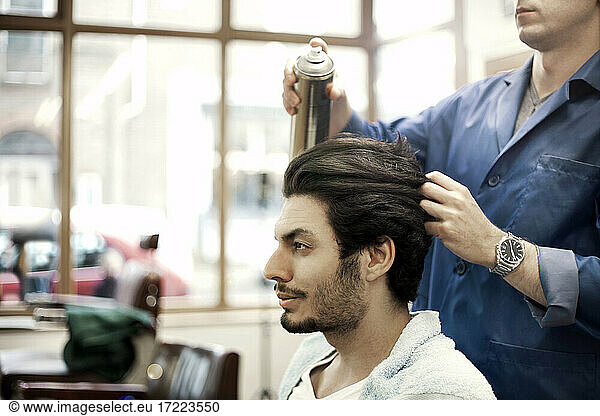 Friseur sprüht Haare eines männlichen Kunden