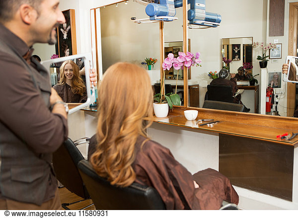 Friseur zeigt Kunden gestylt lange rote Haare im Salon