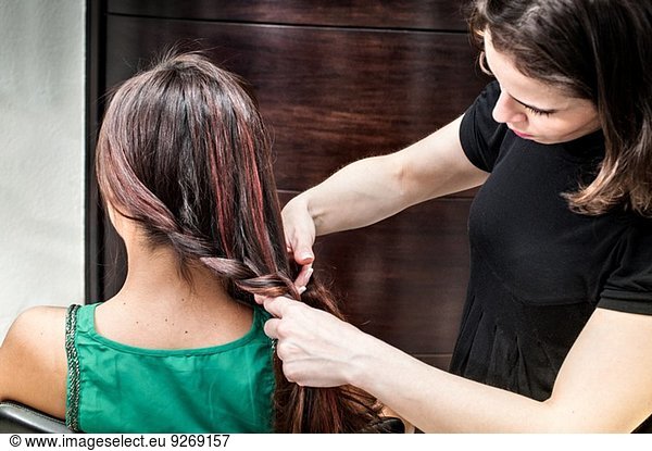Friseurin flechtet lange Haare der jungen Frau im Friseursalon