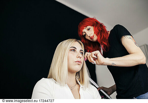 Friseurin mit gefärbten Haaren  die das Haar eines weiblichen Modells im Studio zurechtrückt