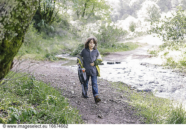Front view concentrated kid walking on trail path by river