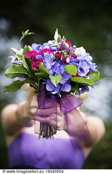 Front view of a teenage girl holding a bouquet of flowers on front of her face.