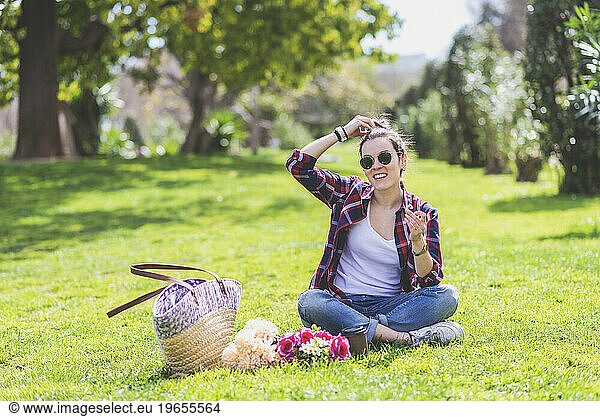 Front view of a young hipster woman sitting on grass in a park w