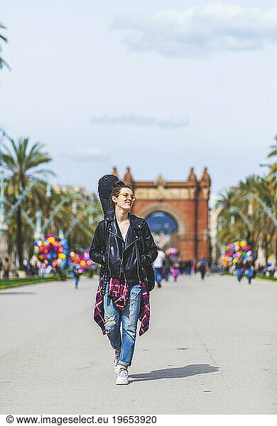 Front view of a young laughing hipster woman walking in a park i