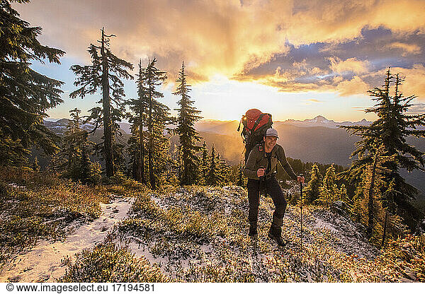 Front view of backpacker hiking over scenic mountain ridge at sunset
