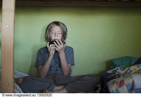 Front view of boy using smart phone while sitting on bed