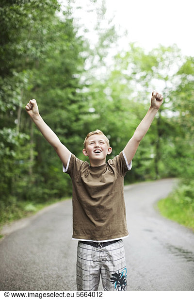 Front view of excited boy with arms raised standing in forest