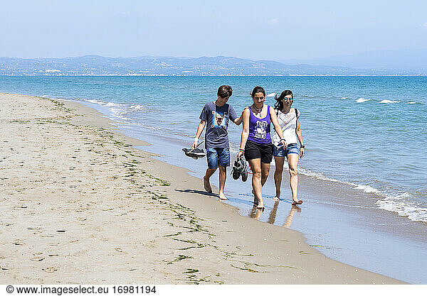 Front view of family walking barefoot on seashore beach on sunny day