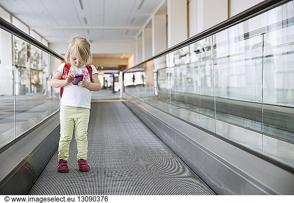 Front view of girl playing with smart phone on moving walkway