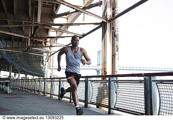 Front view of man running by railing and river against sky