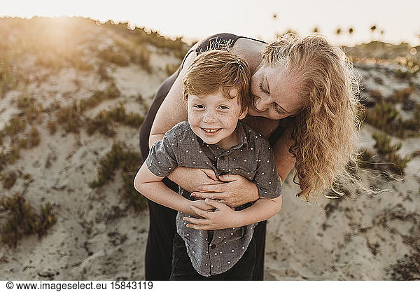 Front view of mother hugging redheaded kindergarten age son at sunset