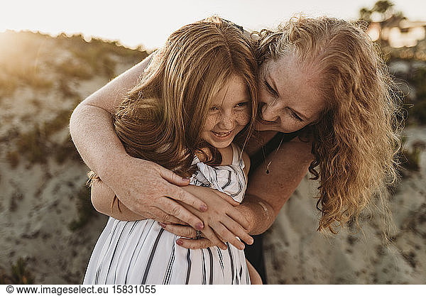 Front view of mother hugging young daughter at beach during sunset