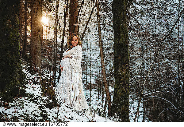 Front view of pregnant woman in the forest with the sun behind her