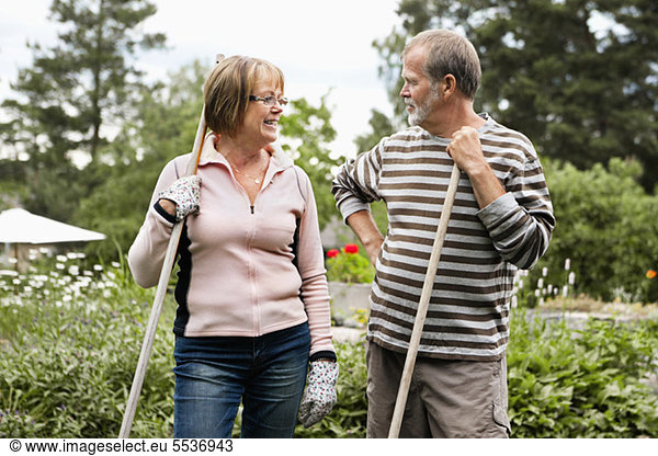 Front view of senior couple standing in back yard with rake
