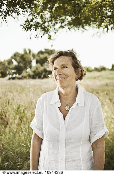 Front view of smiling mature woman standing in grassland