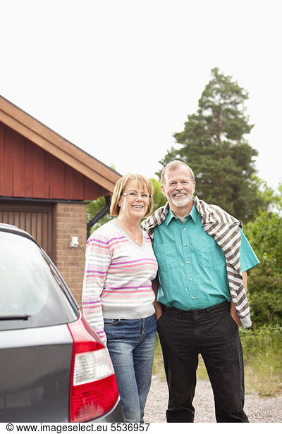 Front view of smiling senior couple standing near car