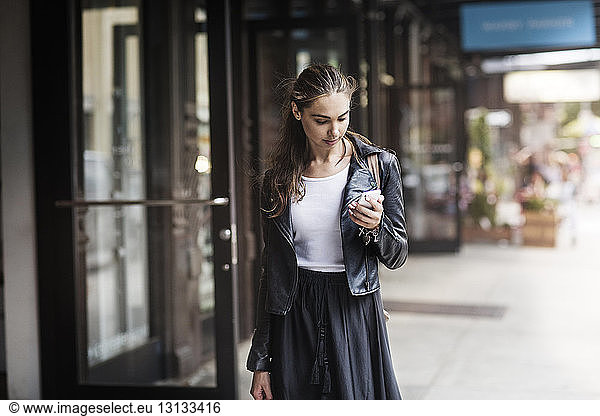 Front view of woman using phone while standing on sidewalk