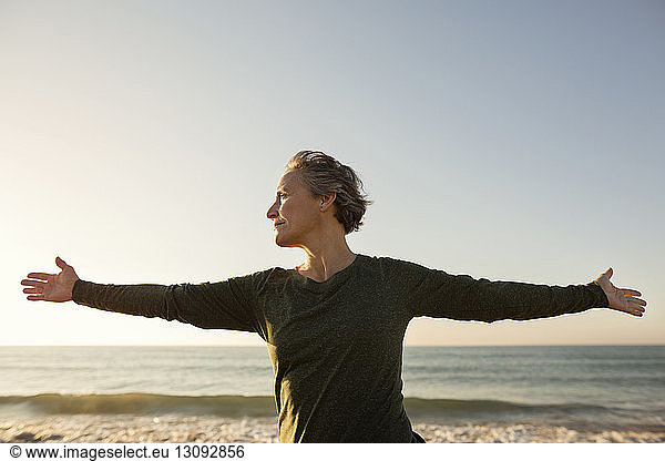 Front view of woman with arms outstretched at beach against clear sky