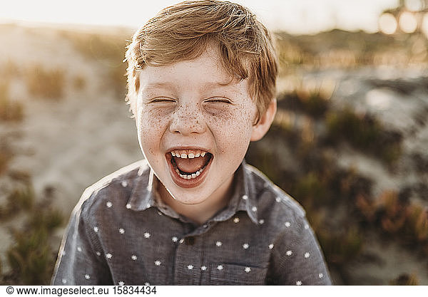 Front view of young kindergarten age boy laughing during beach sunset