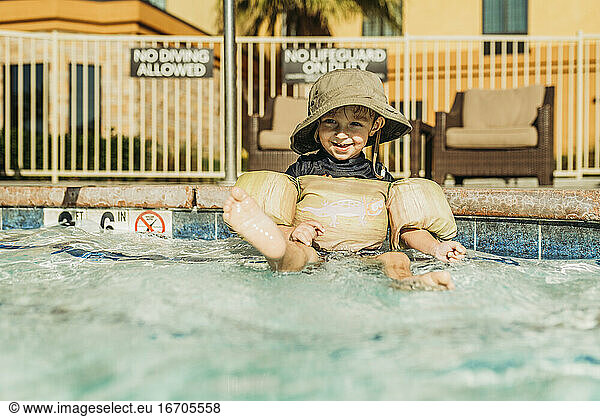 Front view of young toddler boy sitting in hotel pool on vacation