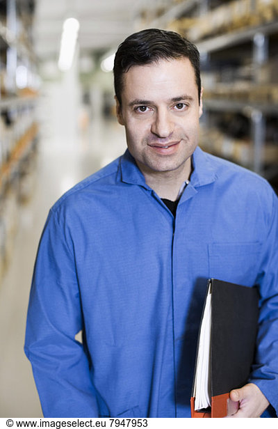 Front view portrait of confident male electrician holding file while standing in industry