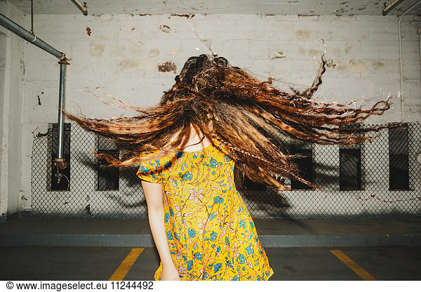 Frontansicht einer jungen Frau  die ihr langes gewelltes Haar auf einem Innenparkplatz schüttelt