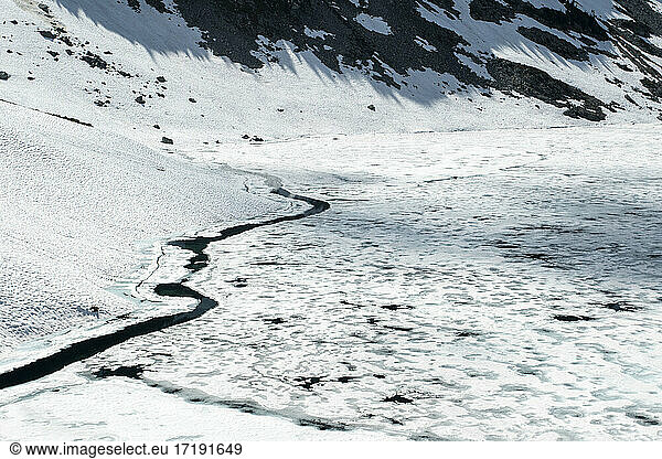 Frozen lake with ice and snowy mountains in spring on outdoor hike